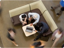 photo from overhead angle of three people working together gathered on a sofa around a laptop computer