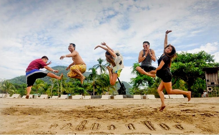 Five people jumping in the air above a Cisco Logo sign written in sand.