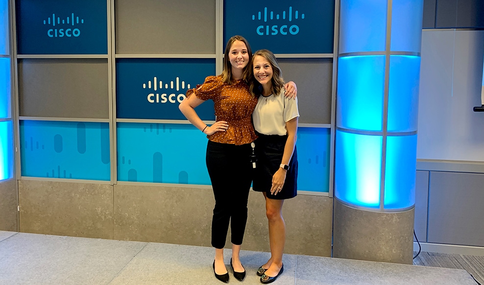 Two people stand next to each other smiling with Cisco logos in the background.