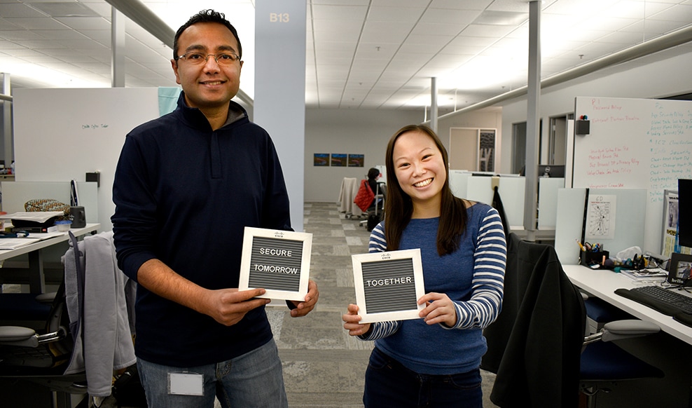 Two people stand in an office space holding up signs that read, 'Secure tomorrow together.'