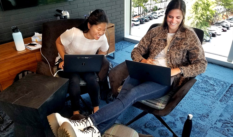 Two people sitting and laughing at something on a laptop screen.