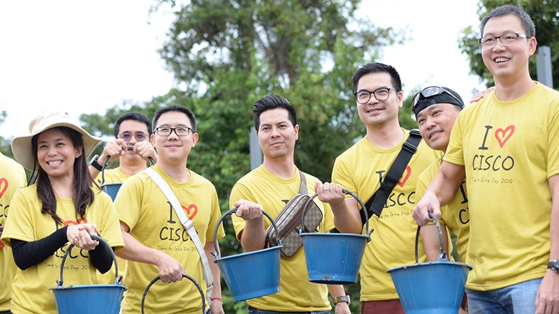 Group of people stand together wearing yellow Cisco shirts and holding buckets.