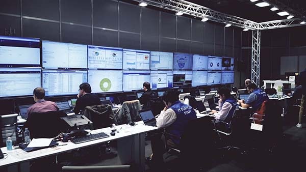 A network operations center with people working on laptops and monitoring screens