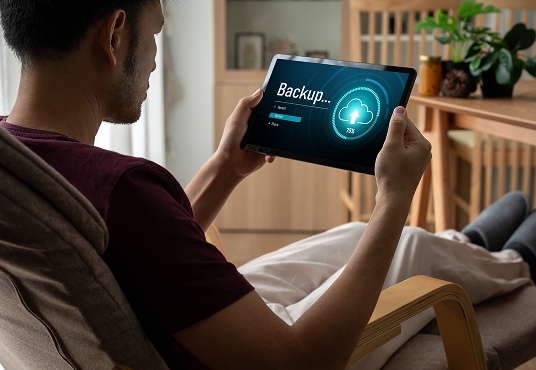 Man sitting in a lounge chair, backing up his tablet.