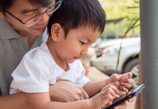 Child and parent looking at a smartphone together outdoors.
