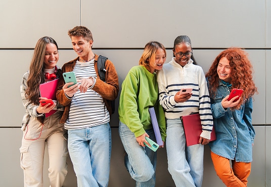 Group of cheerful teens using their smartphones while enjoying their time together.