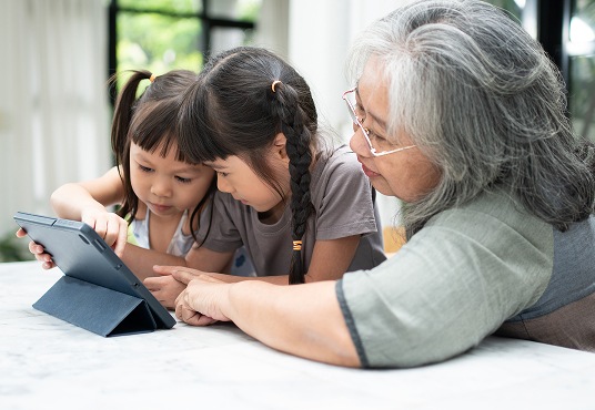 Grandparent with their two grandchildren having fun with a digital tablet at home in the living room.