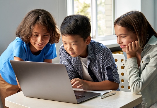 Happy school kids using a laptop together in classroom.