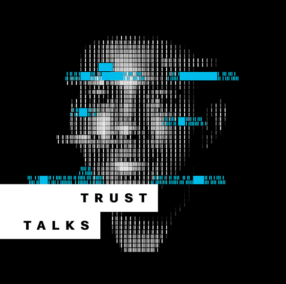 A group of children standing in a circle around a large blue monster mascot in a brightly lit classroom with books and toys on display.