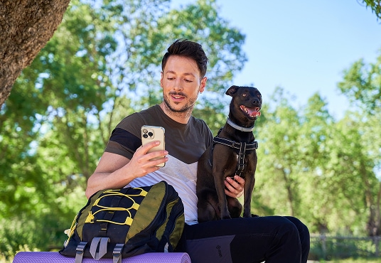 Hiker using a phone and sitting with their dog while resting during a mountain hike.