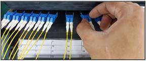 A hand connecting blue and yellow fiber optic cablesDescription automatically generated