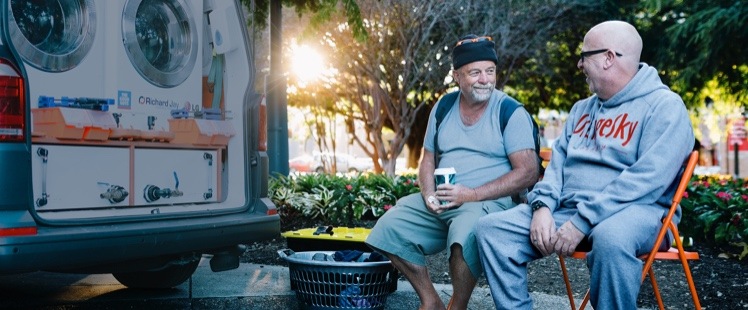 Two men sitting in park by Orange Sky washer truck
