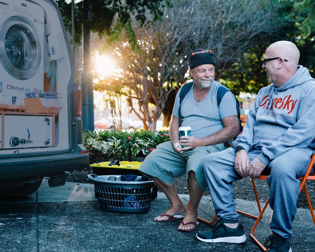 Two men sitting in park by Orange Sky washer truck