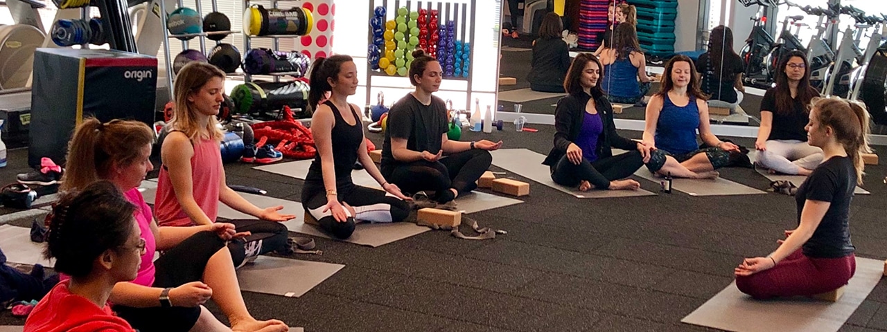 Ten females in a Cisco gym on yoga mats sitting in meditation pose