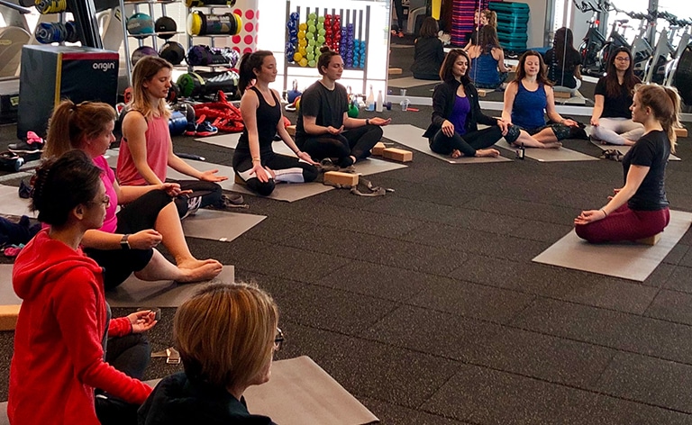 Ten females in a Cisco gym on yoga mats sitting in meditation pose