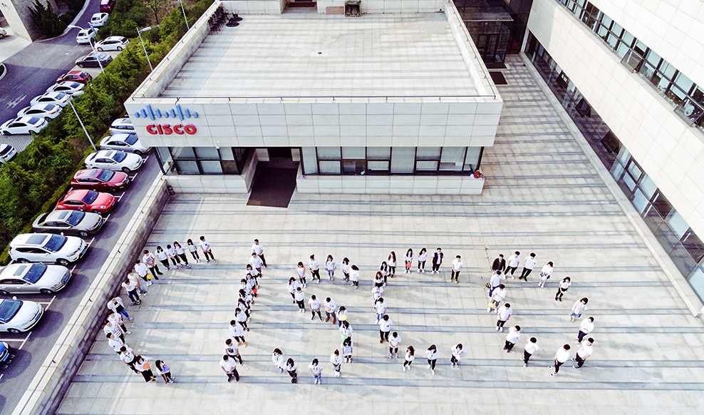 Aerial shot of people dressed in white, forming the word “Cisco” with their bodies.