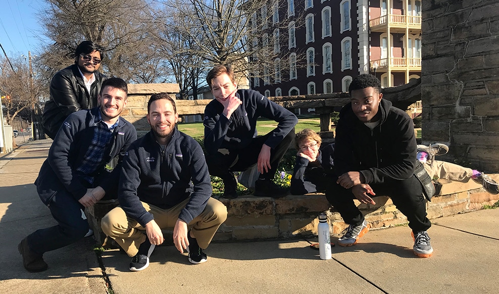 Group of six people pose close to the ground outdoors.