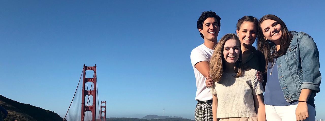 Four people smiling together with the Golden Gate Bridge in the background.