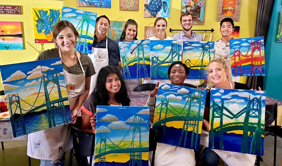 Group of nine people, each holding up a painting of the Golden Gate Bridge.