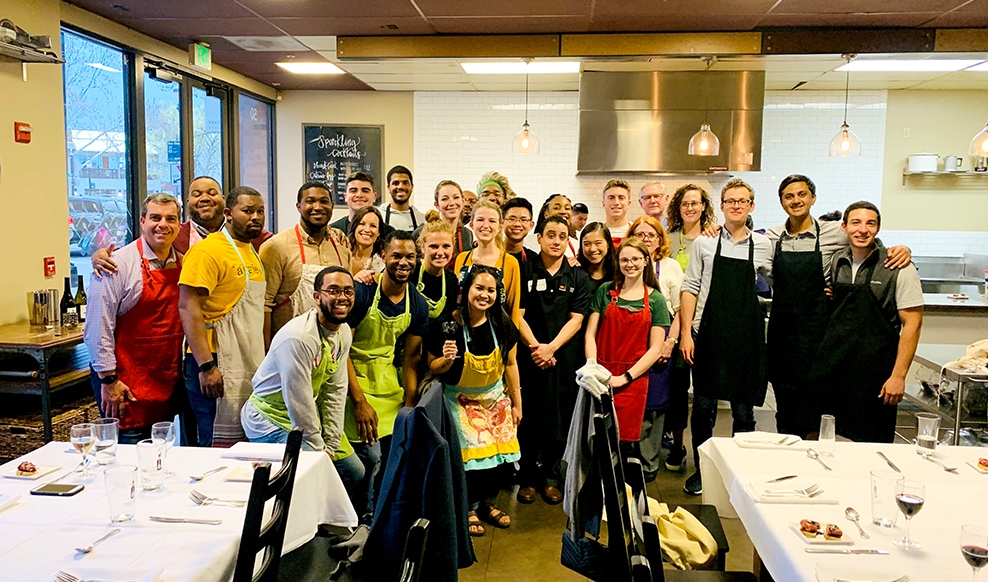 Large group of people wearing aprons huddle together in a kitchen.