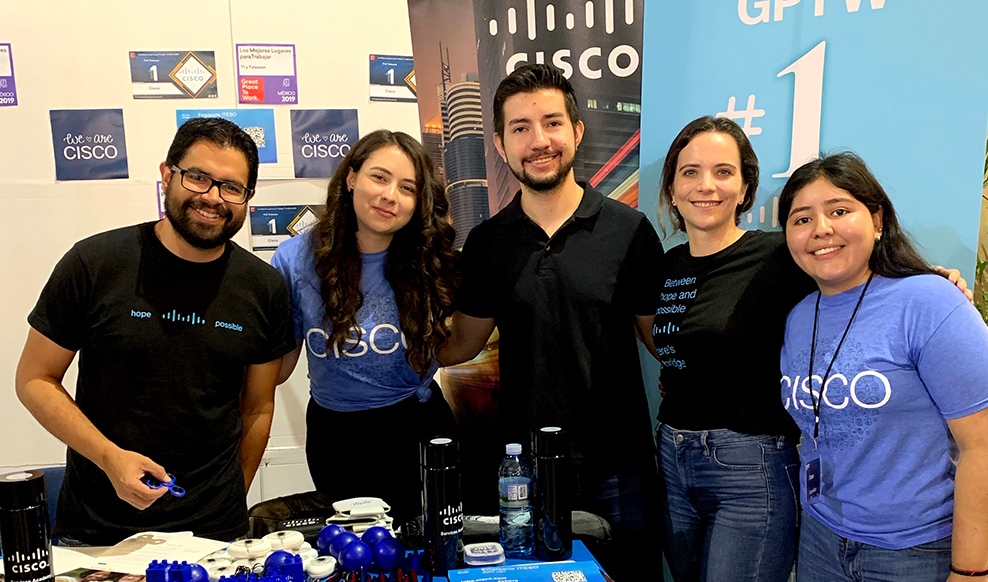 Five smiling people stand together with the Cisco logo in the background.