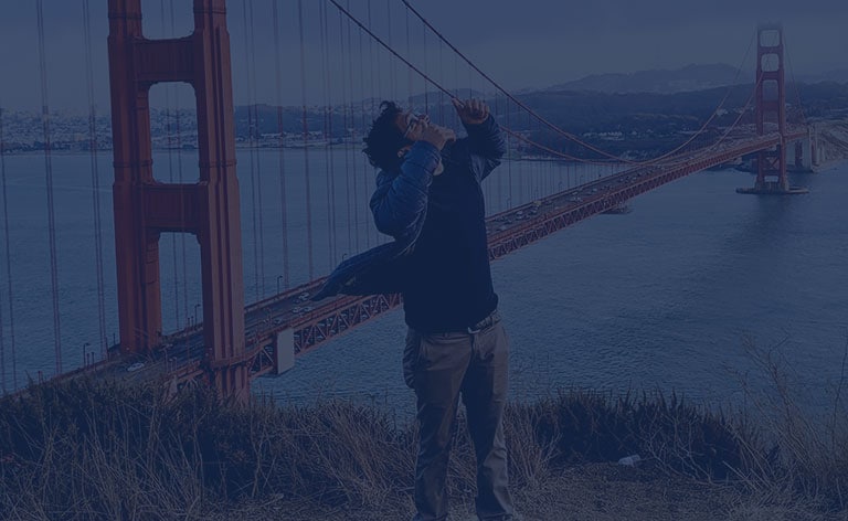 Male holding two thumbs up and looking to the sky with the Golden Gate Bridge and ocean in the background