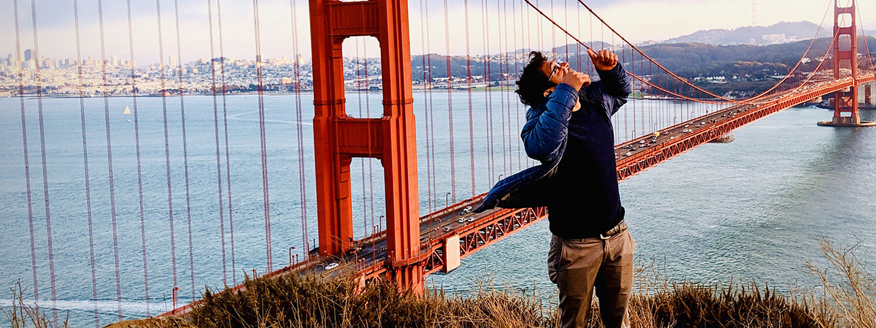 Male holding two thumbs up and looking to the sky with the Golden Gate Bridge and ocean in the background