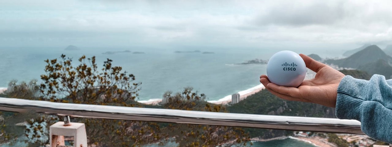 A hand holding a Cisco ball in palm of hand against a mountain and ocean background in Brazil