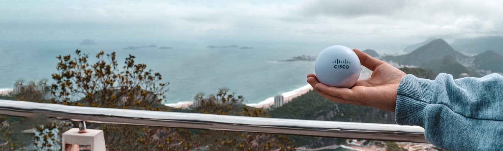 A hand holding a Cisco ball in palm of hand against a mountain and ocean background in Brazil
