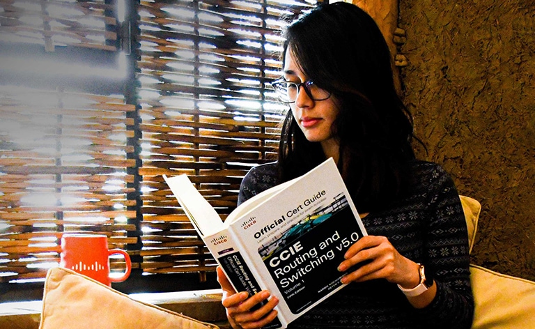 Female sitting criss-cross on a couch looking down at a Cisco Certification Guide Book