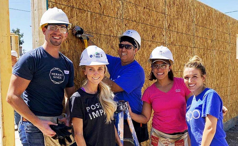 Five employees smiling wearing hard hats as they build a house for a team volunteer event