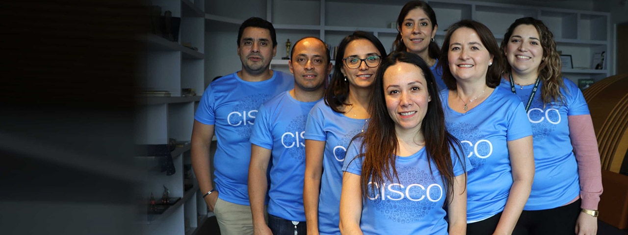 Seven people standing in a triangle formation smiling and wearing the same Cisco shirt.
