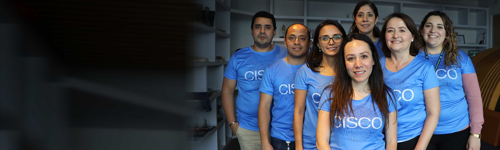 Seven people standing in a triangle formation smiling and wearing the same Cisco shirt.