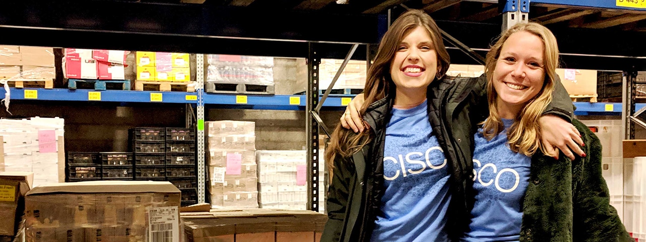 Two females wearing the same blue Cisco shirt volunteering at a food bank sorting produce