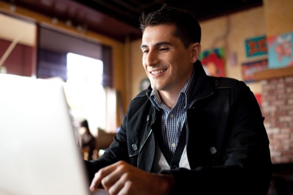 Homem sorrindo enquanto trabalha no computador em uma cafeteria