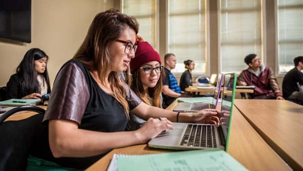 Zwei Studierende, die in einem Kursraum an einem Laptop sitzen.