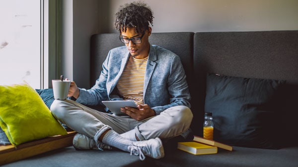 Mann, der mit Kaffee und iPad auf dem Sofa entspannt