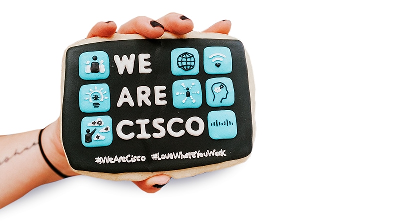 Hand holds a black, blue, and white rectangular cookie that reads, “We Are Cisco.”