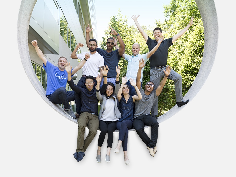 Nine people raising their arms while sitting in a large circular opening.