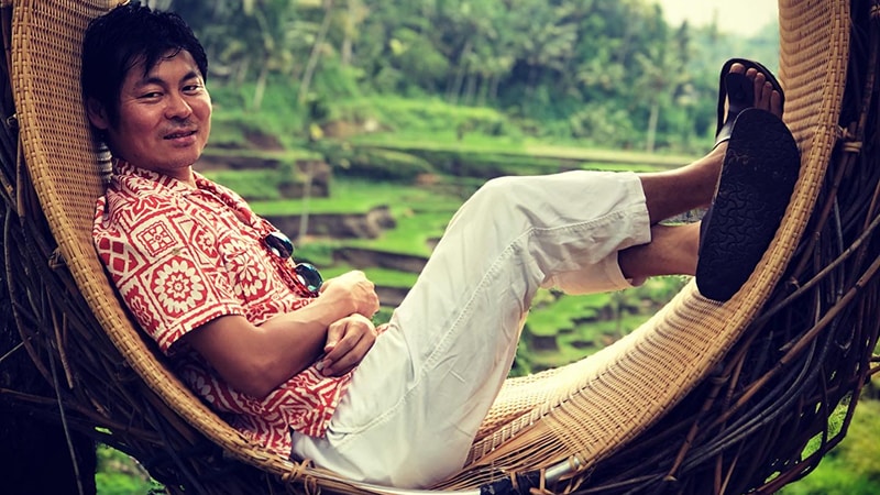 Person reclines in a curved rattan chair.