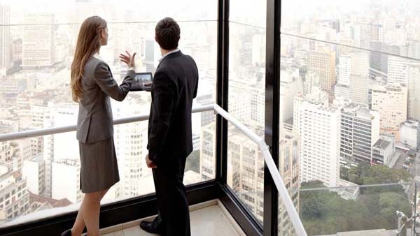 Two people talk while looking out over city buildings