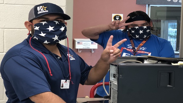 Two people wearing face masks making the peace sign with their fingers