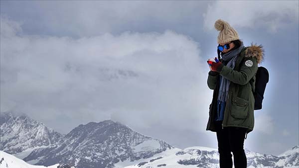 A woman stands on a mountain in the Swiss Alps and uses a mobile phone