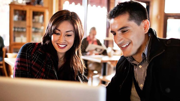 A man and a woman looking into a computer screen and smiling