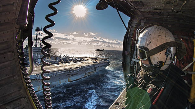 Man sitting in helicopter looking at navy ship
