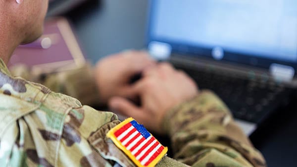 Man in military fatigues using computer with flag patch visible on shoulder