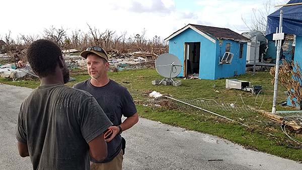 Two people talk in the street next to storm-impacted houses