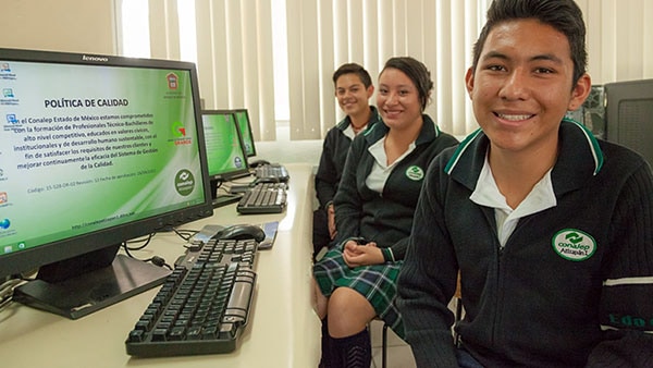 Three Networking Academy students smiling next to desktop computers