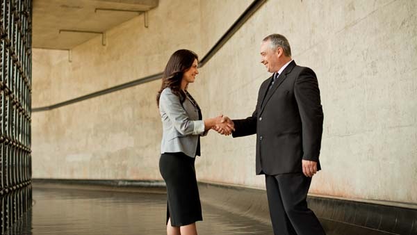 Two people, dressed in business attire, shaking hands.