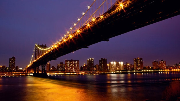 Illuminated suspension bridge over water at night with city in distance